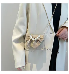Detail of beige mini crossbody bag featuring a champagne bow and pearl decoration on a suit