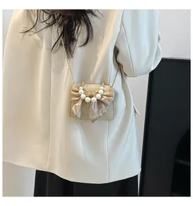 Detail of elegant beige crossbody bag with pearl handle and large satin bow decoration
