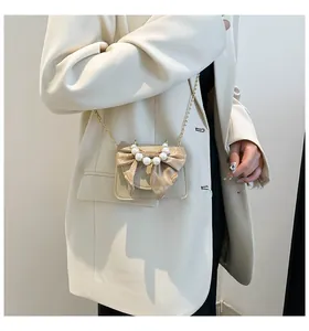 Detail of elegant crossbody bag featuring a silk bow with pearl accents and gold chain