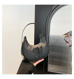 Detail of black crescent shoulder bag featuring 3D letters and gold metal hardware