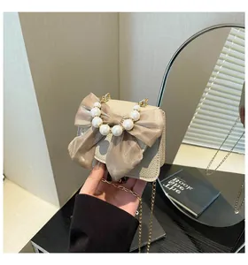 Detail of cream leather mini bag with large champagne satin bow and pearl handle strap