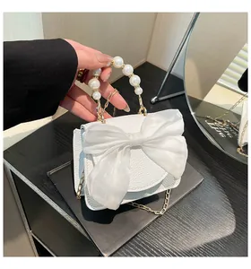 Close-up of white mini handbag with gauze bow, pearl handle, and gold chain strap