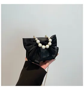 Detailed view of elegant black handbag featuring a large fabric bow and decorative pearl handle
