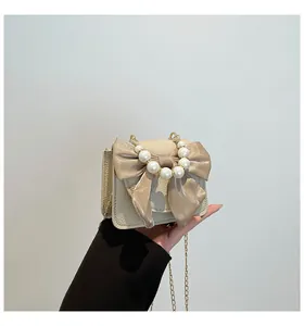 Close-up of cream mini bag featuring large satin bow, pearl handle, and gold chain strap