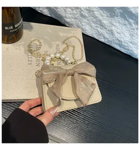 Close-up of mini crossbody bag with satin bow, pearl handle and gold chain strap