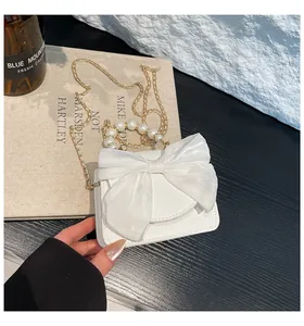 Close-up of white mini bag with large organza bow, pearl handle, and gold chain strap