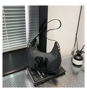 Detail of the embossed black SM logo on a sleek faux leather crescent shoulder bag