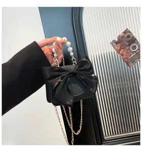 Detail of black leather bag with pearl handle, silk bow, and gold chain strap