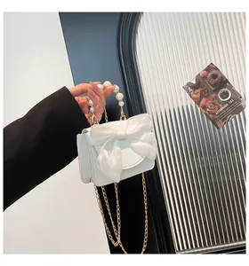 Detail of white mini bow handbag with pearl handle and golden chain on a textured surface