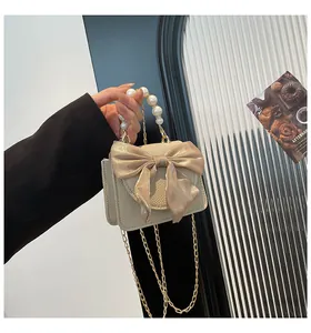 Detail of off-white mini bag with satin bow, pearl handle and gold chain strap