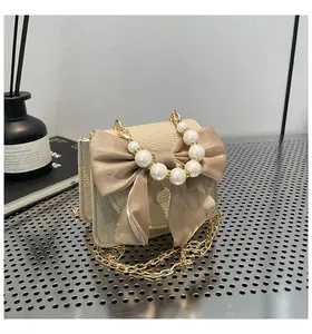 Detail of cream leather mini bag with silk bow and pearl handle on metal background