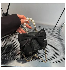 Detail of black pebbled leather crossbody bag with silk bow and large faux pearl handle