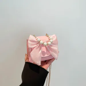 Pink crossbody bag with large satin bow and faux pearl handle shown in hand