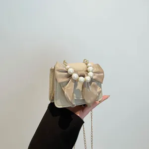 Elegant beige crossbody bag featuring a large satin bow and beaded pearl handle