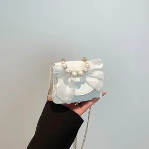 Mini white crossbody bag with tulle bow and pearl handle shown in hand, elegant design