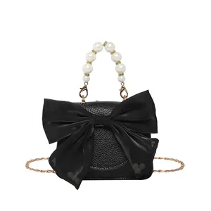 Black leather crossbody bag with oversized bow, pearl handle, and gold chain strap