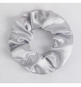 Makro-Detail von silbernem Satin-Haargummi mit glänzender Seidenstruktur und Falten