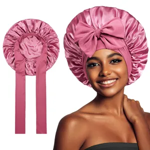 Pink satin bonnet for long hair with a large bow and adjustable straps on white background