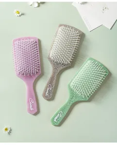 Three colorful square cushion hairbrushes with mandala patterns on a fresh floral background