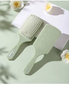 Detail view of mint green paddle brush with white floral lace patterns and soft massage bristles