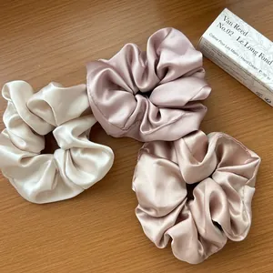 Dettaglio ravvicinato di tre elastici per capelli in raso setoso in crema, rosa e oro