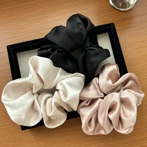 Dettaglio di tre grandi elastici per capelli in raso nero, beige e champagne in tessuto di seta