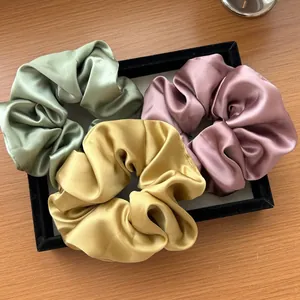 Dettaglio di tre elastici per capelli in raso verde giallo e rosa su un vassoio di velluto