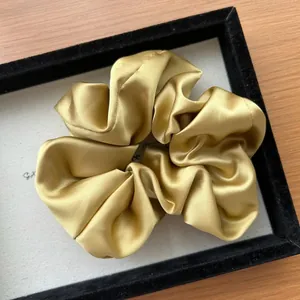 Dettaglio dell'elastico per capelli in raso dorato con texture setosa e pieghe eleganti