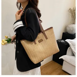 Détail d'un grand sac cabas en paille avec anses en cuir marron et patch logo central
