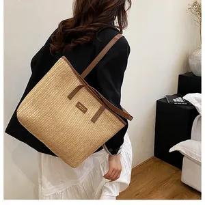 Détail du sac cabas en paille tressée avec anses en cuir marron et étiquette de marque