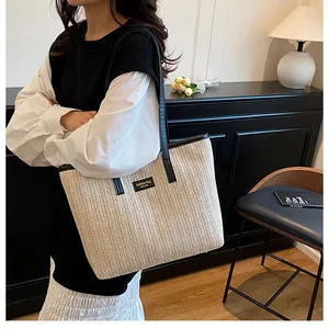 Détail du sac cabas en paille tissée avec bordure en cuir noir et plaque logo
