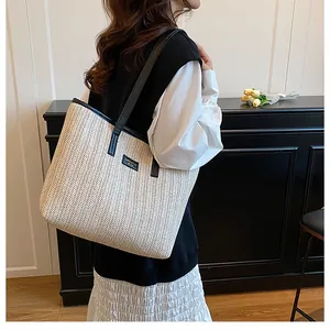 Détail du sac cabas en paille tressée avec lanières en cuir noir et écusson de la marque