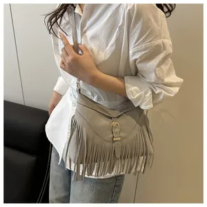 Primer plano de bolso bandolera bohemio gris claro con flecos usado con ropa casual