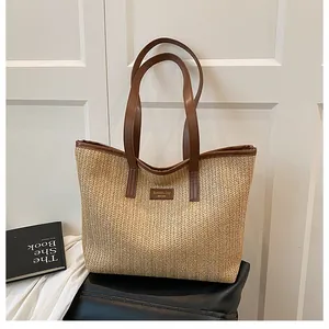 Détail d'un sac cabas en paille tressée avec anses en cuir marron et patch logo