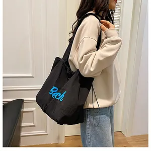 Gros plan du sac cabas noir en toile avec broderie bleue Bech porté par un mannequin