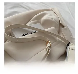Detail of cream leather handbag with adjustable thin strap and gold metal hardware accents