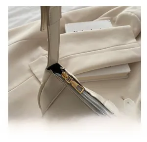 Detail of a smooth golden metal zipper on a beige leather baguette shoulder bag