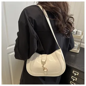 Close-up of a white patent leather hobo bag with gold metal clasp on model's shoulder