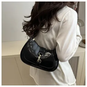 Detail of glossy black leather underarm bag featuring metallic hook accents on the strap