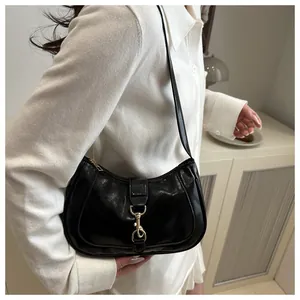 Detail of black glossy faux leather hobo bag featuring a golden metallic hook closure