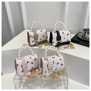 Détail de mini sacs à imprimé cerise avec poignées en perles et bandoulières dorées