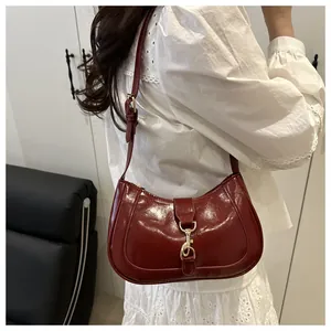 Detail of burgundy glossy leather hobo bag with vintage gold buckle on model shoulder