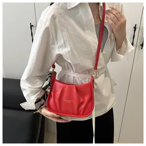 Détail d'un sac bandoulière rouge plissé avec un foulard décoratif noir et blanc