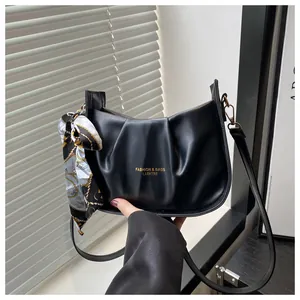 Détail d'un sac à bandoulière plissé noir avec foulard décoratif et logo texte doré