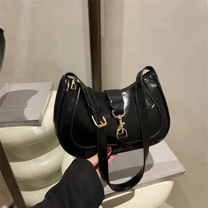 Glossy black crescent underarm bag with gold hardware on a minimalist display
