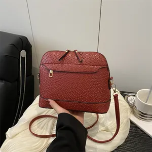 Deep red woven crossbody bag with dual zippers and wide shoulder strap in lifestyle setting