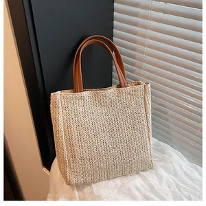 Close-up of minimalist straw tote bag with woven texture and brown leather handles