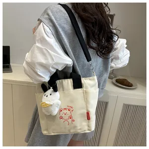 Détail du sac cabas en toile avec imprimé ours et breloque lapin en peluche sur l'épaule