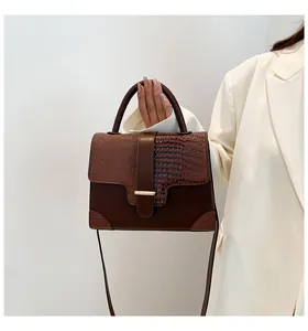 Détail d'un sac à main marron foncé avec textures mates et croco et boucle dorée élégante