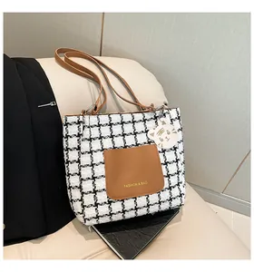 Close-up of houndstooth tote bag with brown leather pocket and white tiger charm